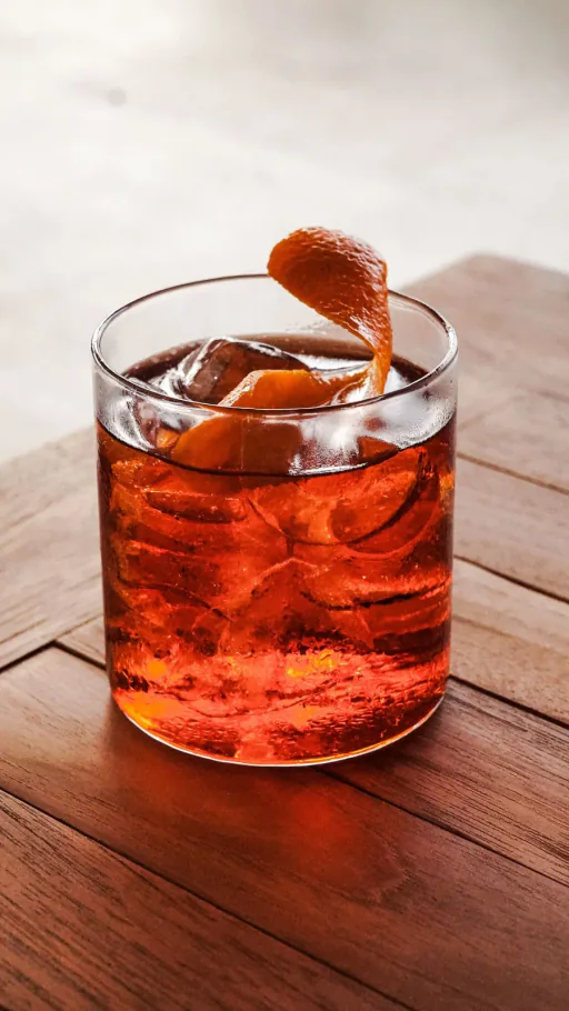 Negroni com gelo e casca de laranja em copo baixo sobre mesa de madeira